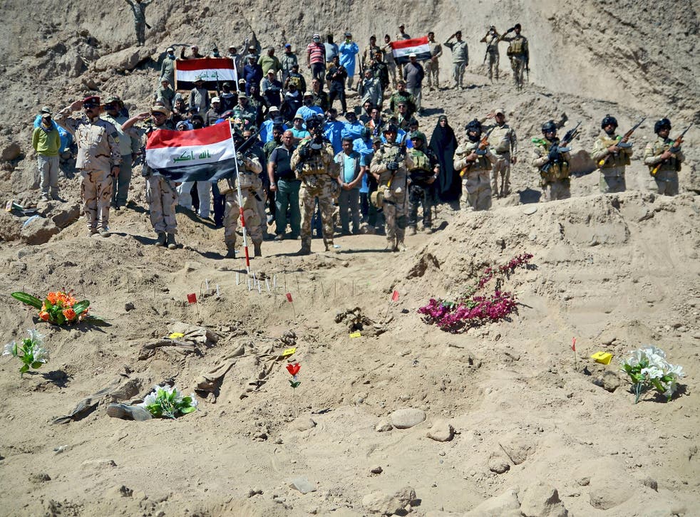 Iraqi soldiers salute as they stand next to a mass grave containing the bodies of hundreds of Shia soldiers from Camp Speicher who were killed by Isis militants in Tikrit