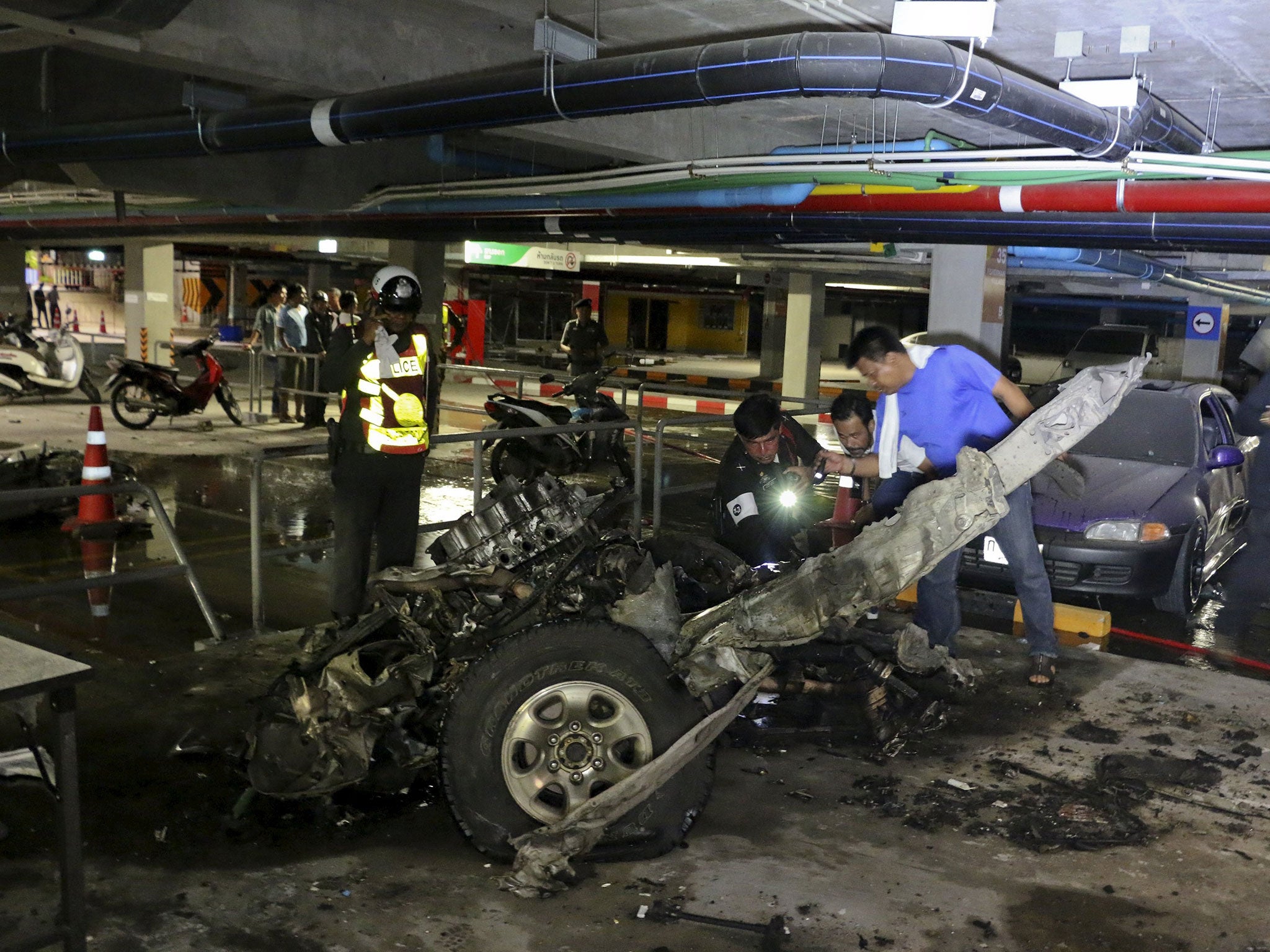 Police officers inspect the remains of the car after the bombing at the shopping mall in Koh Samui, Thailand