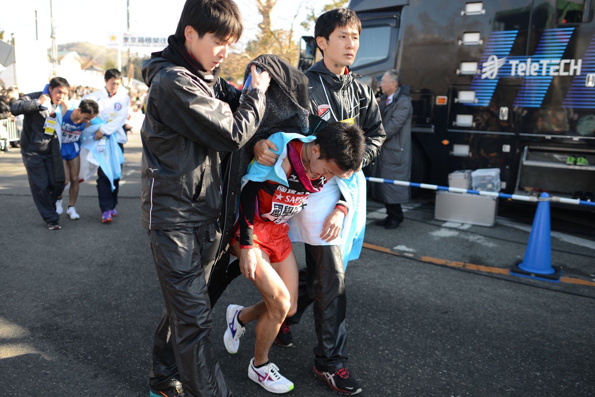 Two Hakone runners are helped by teammates after completing the final leg on day one