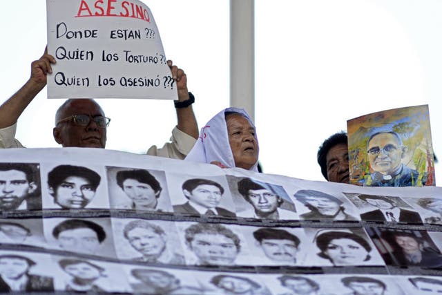 People hold a poster with portraits of disappeared people and a sign reading "Assassin. Who tortured them? Who killed them?"