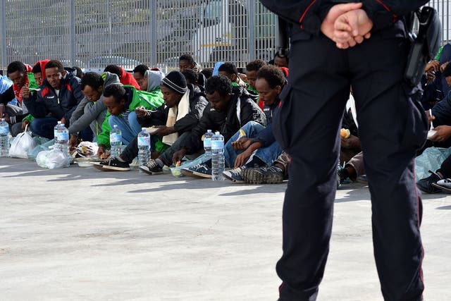 An Italian policeman stands guard as migrants eat while waiting at the port of Lampedusa to board a ferry bound for Porto Empedocle in Sicily. Authorities on the Italian island of Lampedusa struggled to cope with a huge influx of newly-arrived migrants as