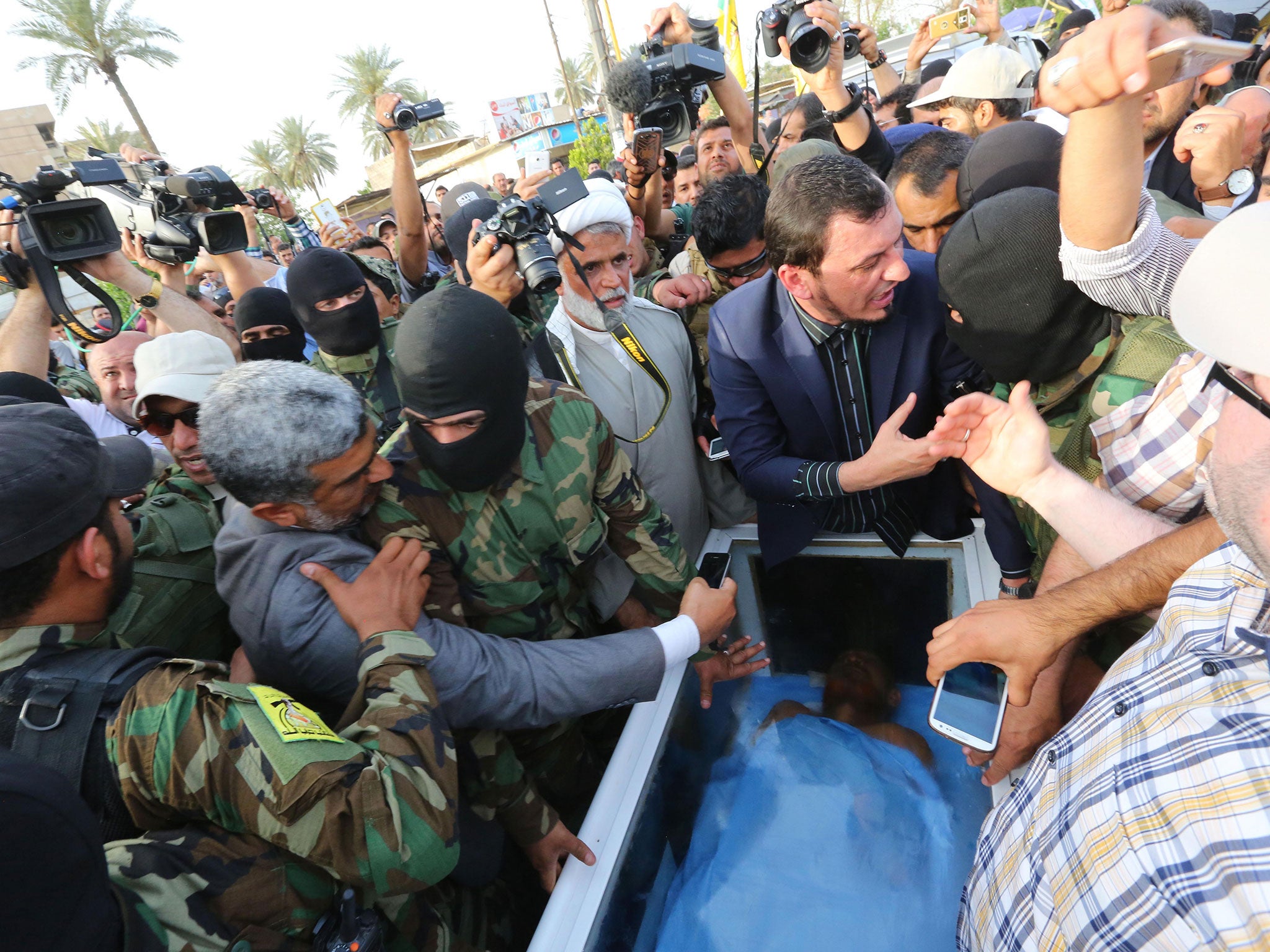 Civilians and members of the Iraqi Hezbollah Brigades gather around a glass-topped coffin as they prepare to deliver what they claim is the body of former Saddam Hussein deputy Izzat Ibrahim al-Douri to the Ministry of Health in the Karrada neighborhood o