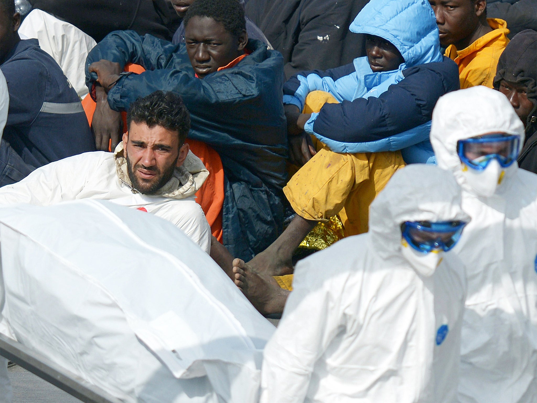 Mohammed Ali Malek, surrounded by some of his surviving ‘cargo’ of migrants after their rescue off Libya, watches rescuers carry a body from an Italian Coast Guard vessel in Malta