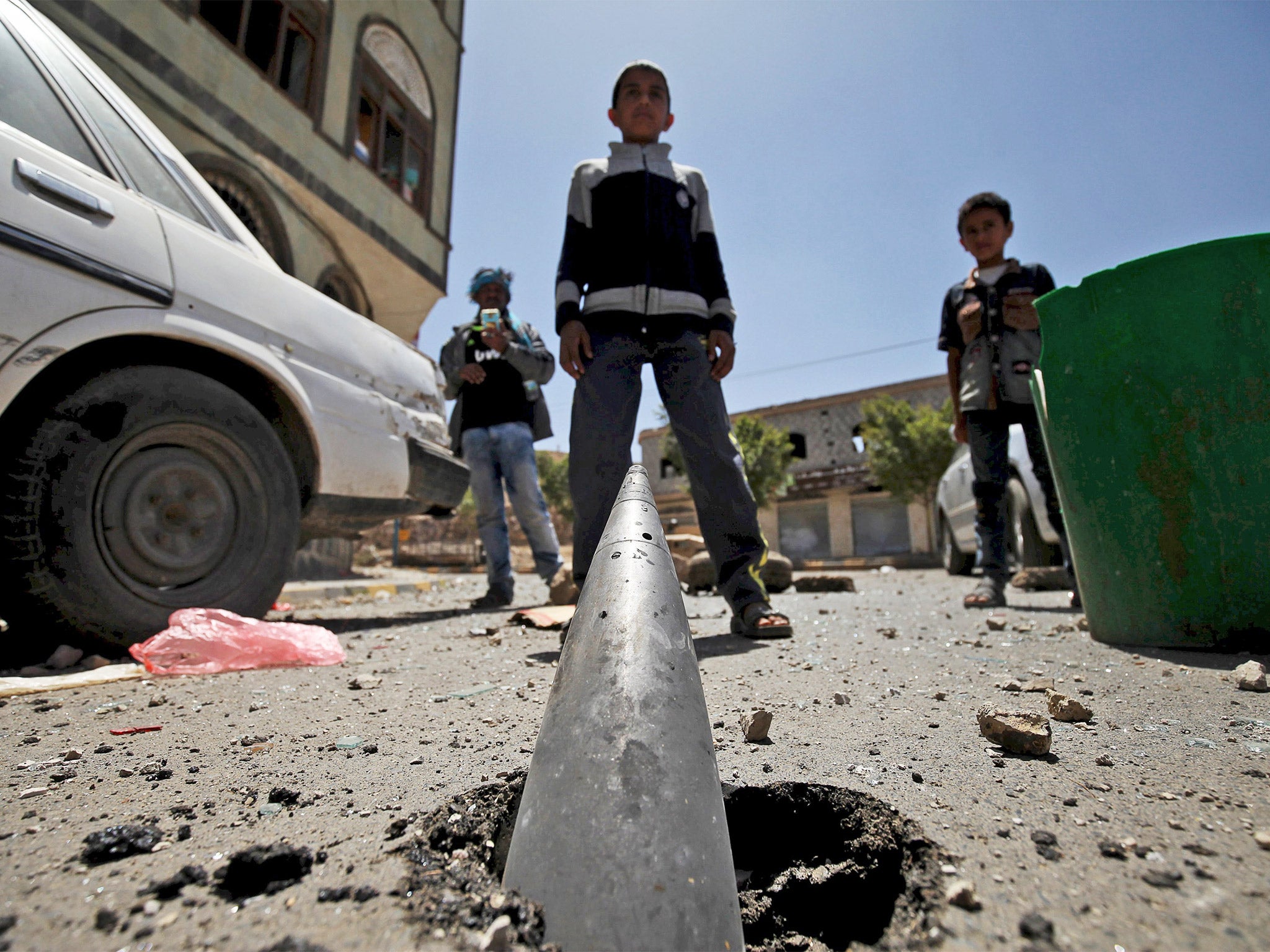 Boys stand in front of a partially buried artillery shell after an air strike on Sanaa