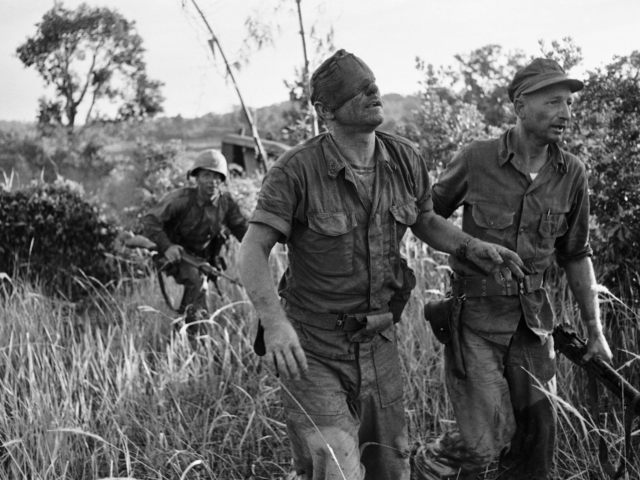 A US Marine, who was wounded in the head as he fought against the Viet Cong from inside an amphibious tank, is led to evacuation helicopter landing zone at Van Tuong, Vietnam on 19 August 1965