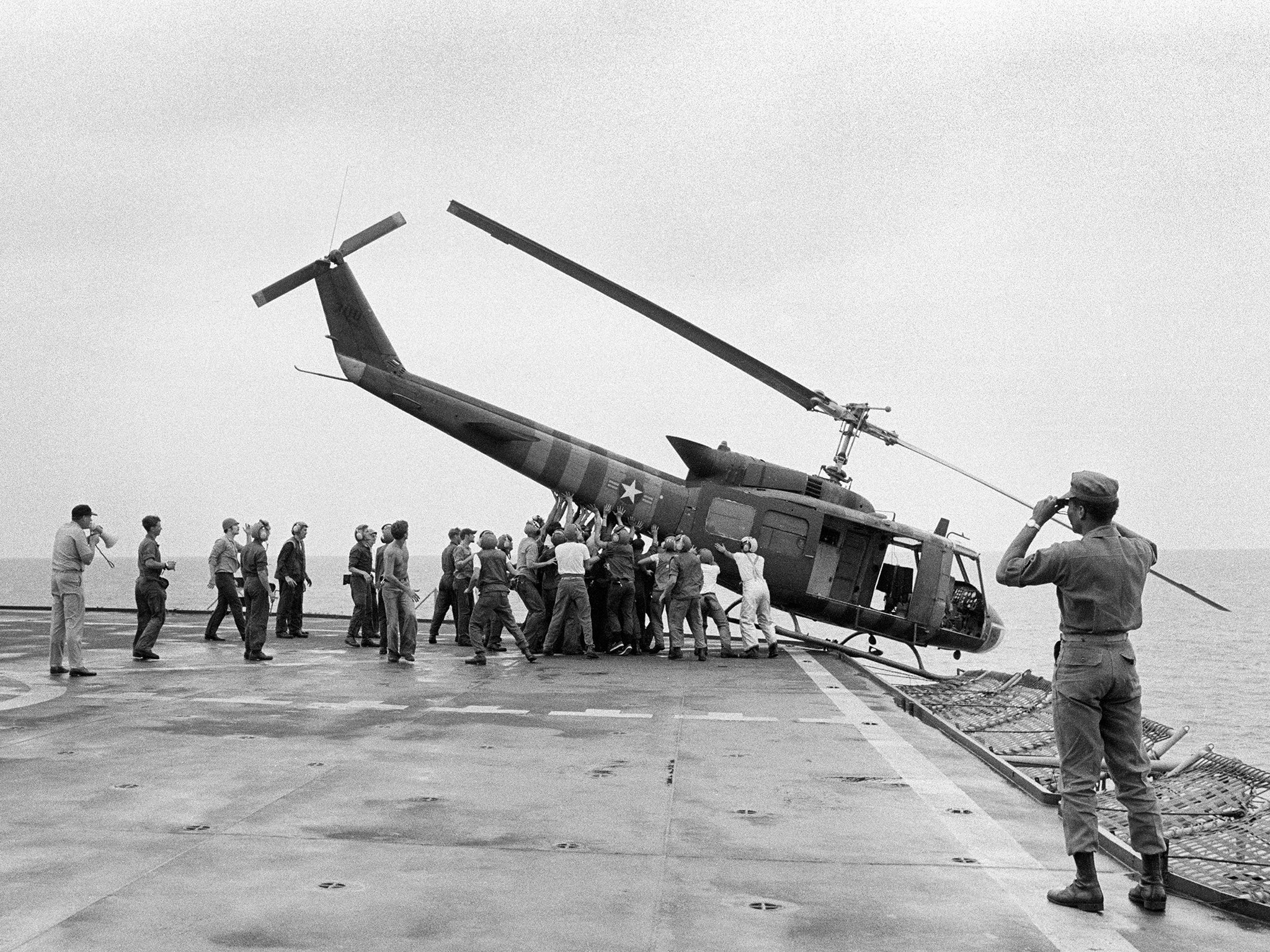 US Navy personnel aboard the USS Blue Ridge push a helicopter into the sea in order to make room for more evacuation flights from Saigon (AP)