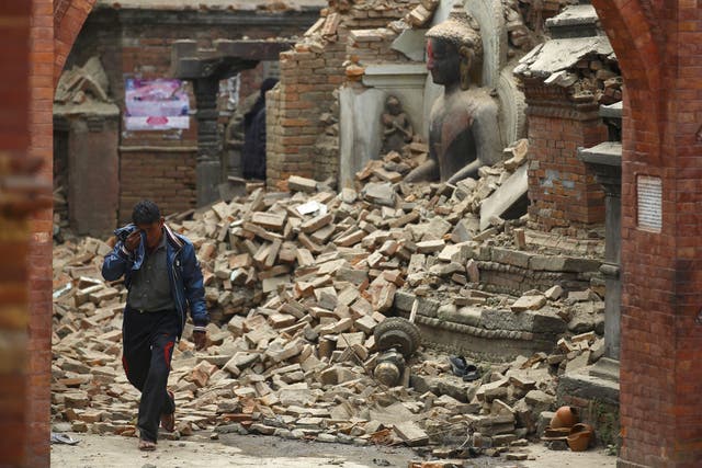 A man cries as he walks on the street while passing through a damaged statue of Lord Buddha a day after the earthquake in Bhaktapur, Nepal 