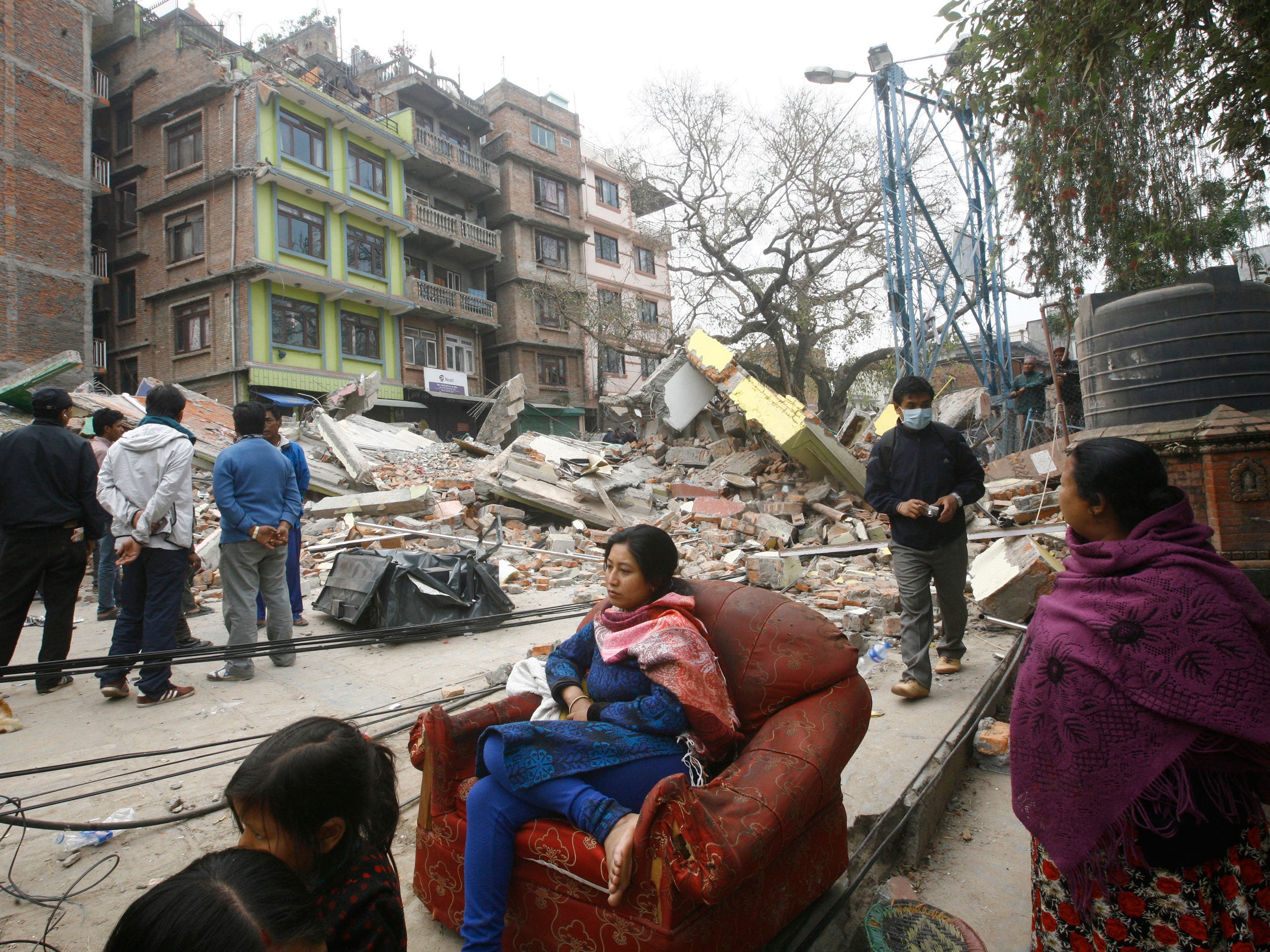 A Nepalese woman sits on a sofa outdoors surrounded by the debris of Saturday's earthquake