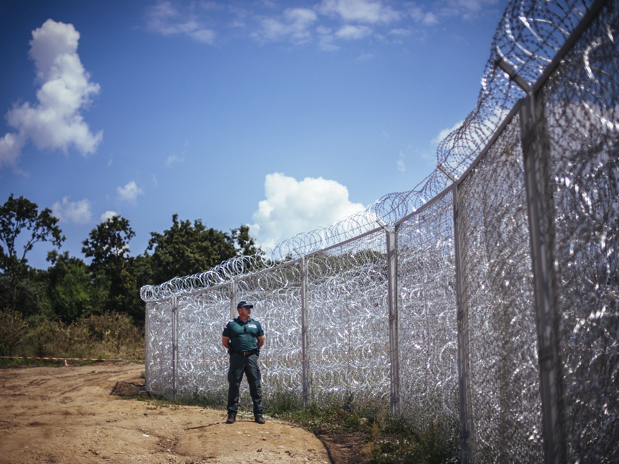 A border policeman stands next to a barbed wire wall on the Bulgarian border with Turkey, near the village of Golyam Dervent