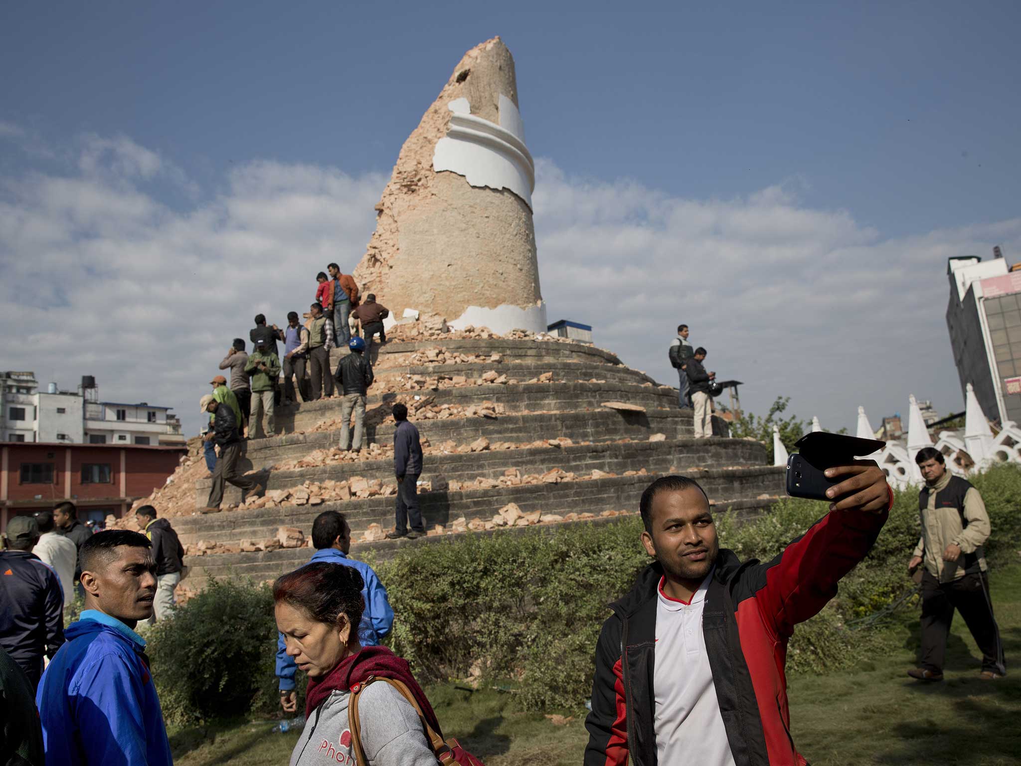 A man appears to take a selfie in front of the destroyed Dharahara Tower