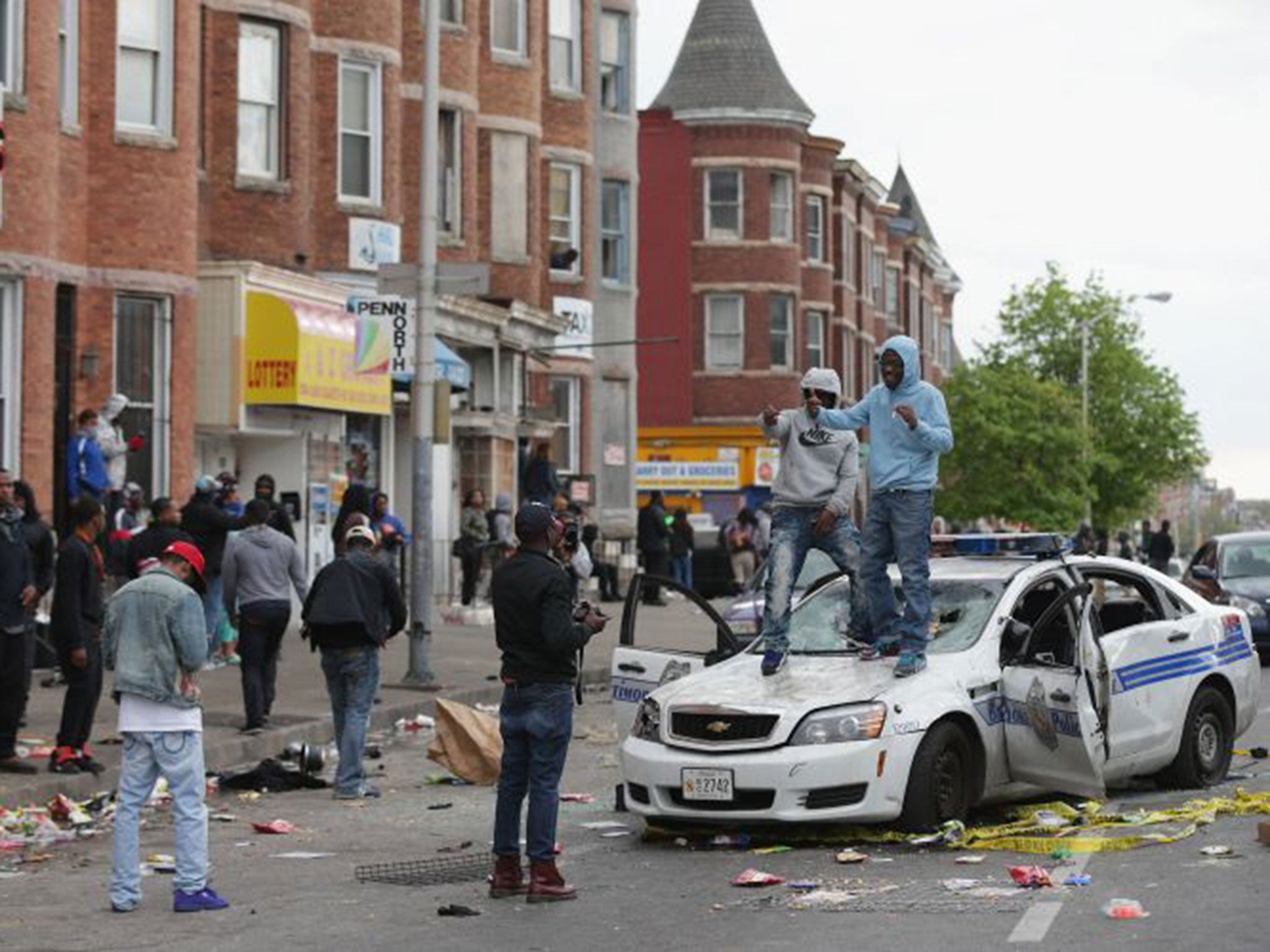 People pose for photographs on the hood of a Baltimore Police car destroyed by demonstrators