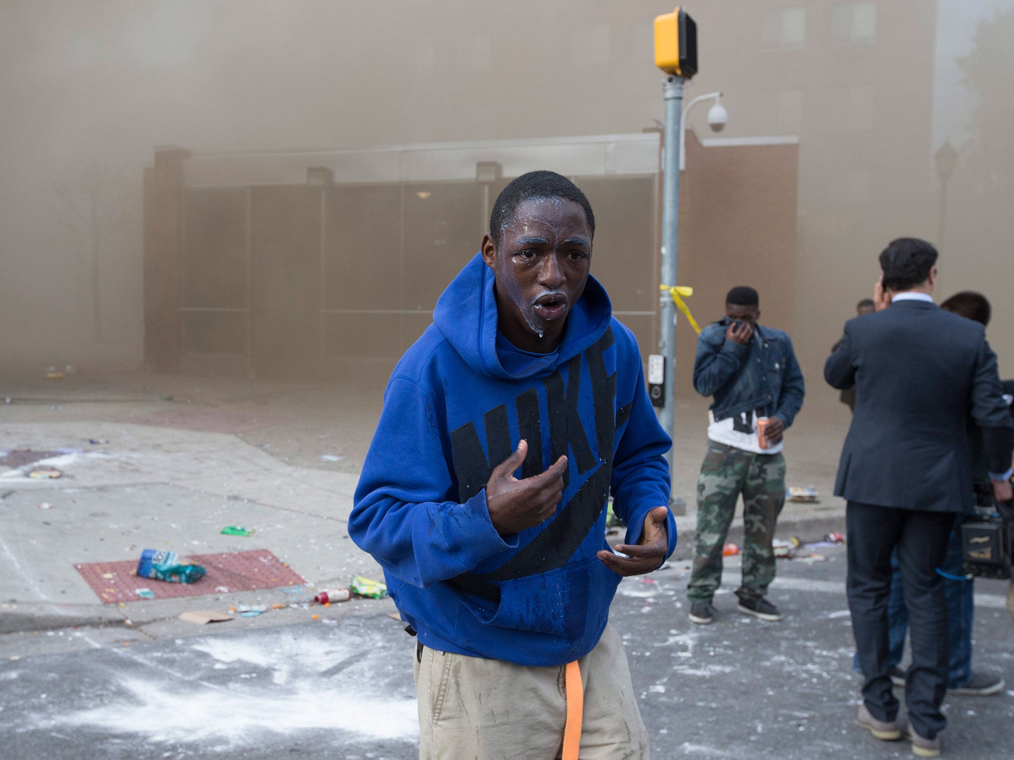 A youth washes out pepper spray from his eyes near a building that caught fire after being looted