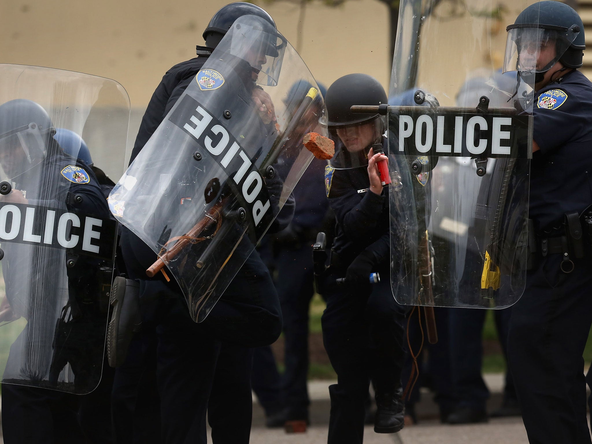 Baltimore Police officers protect themselves as protesters throw broken bricks at them