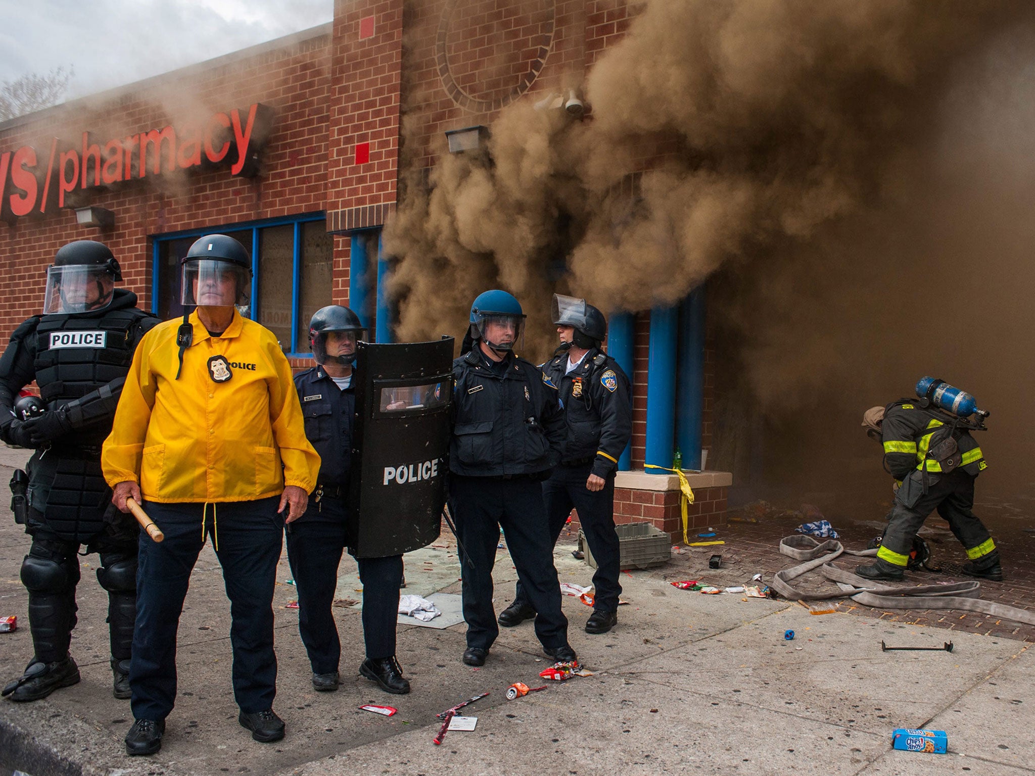 Police stand by a CVS that was on fire as firefighters arrive to fight the blaze