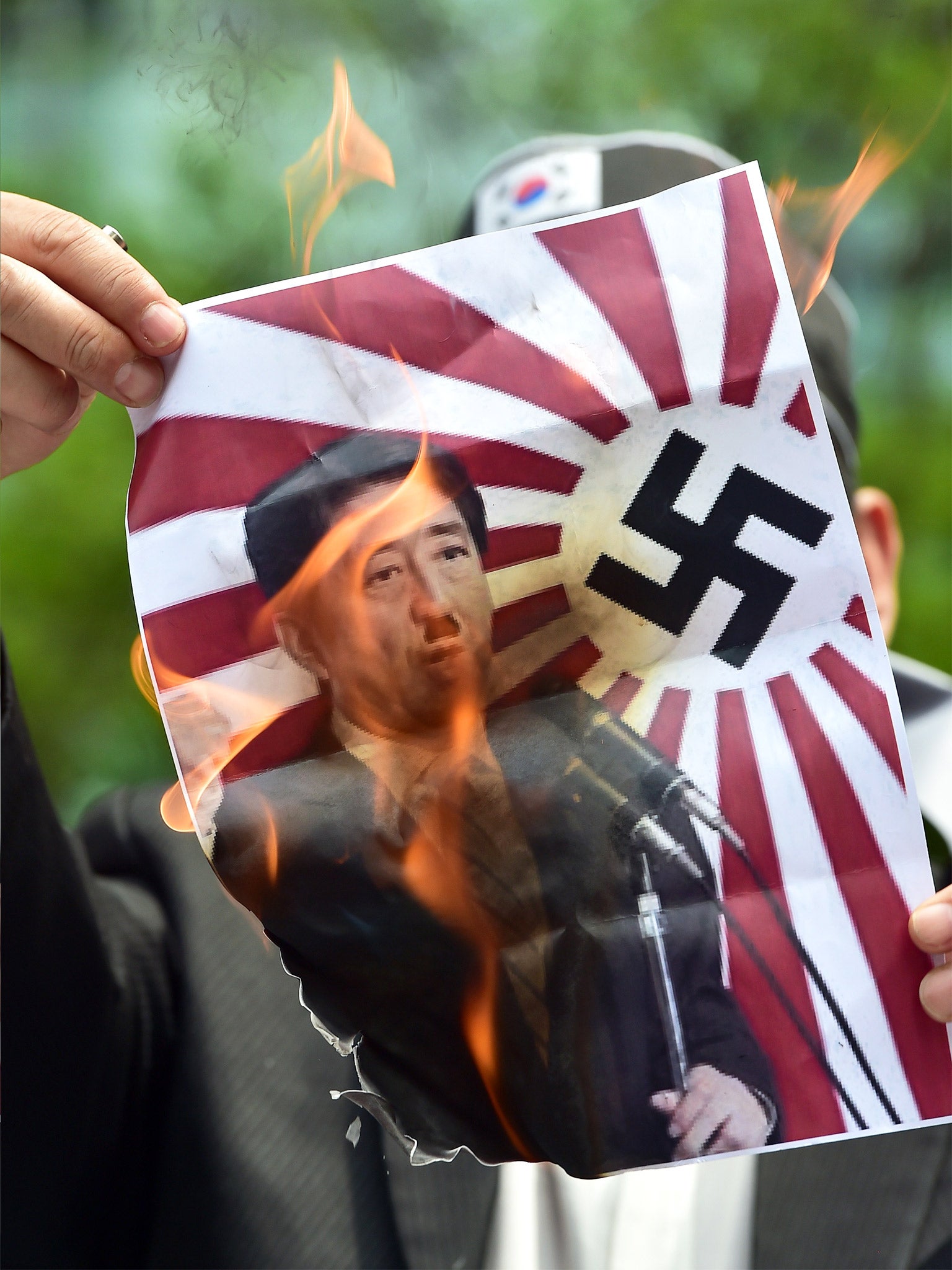 A South Korean activist burns a picture depicting Shinzo Abe as Adolf Hitler during a protest denouncing the Japanese Prime Minister's visit to the US, outside Japan's embassy in Seoul (Getty)