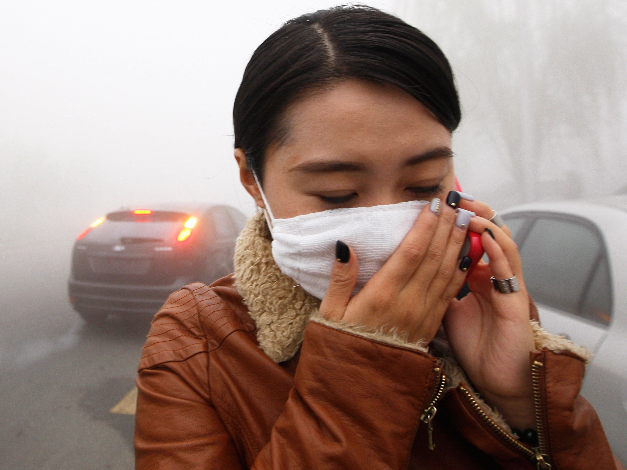 A woman wearing a mask covers her mouth with her hands as she walks through smog in Harbin, northeast China's Heilongjiang province