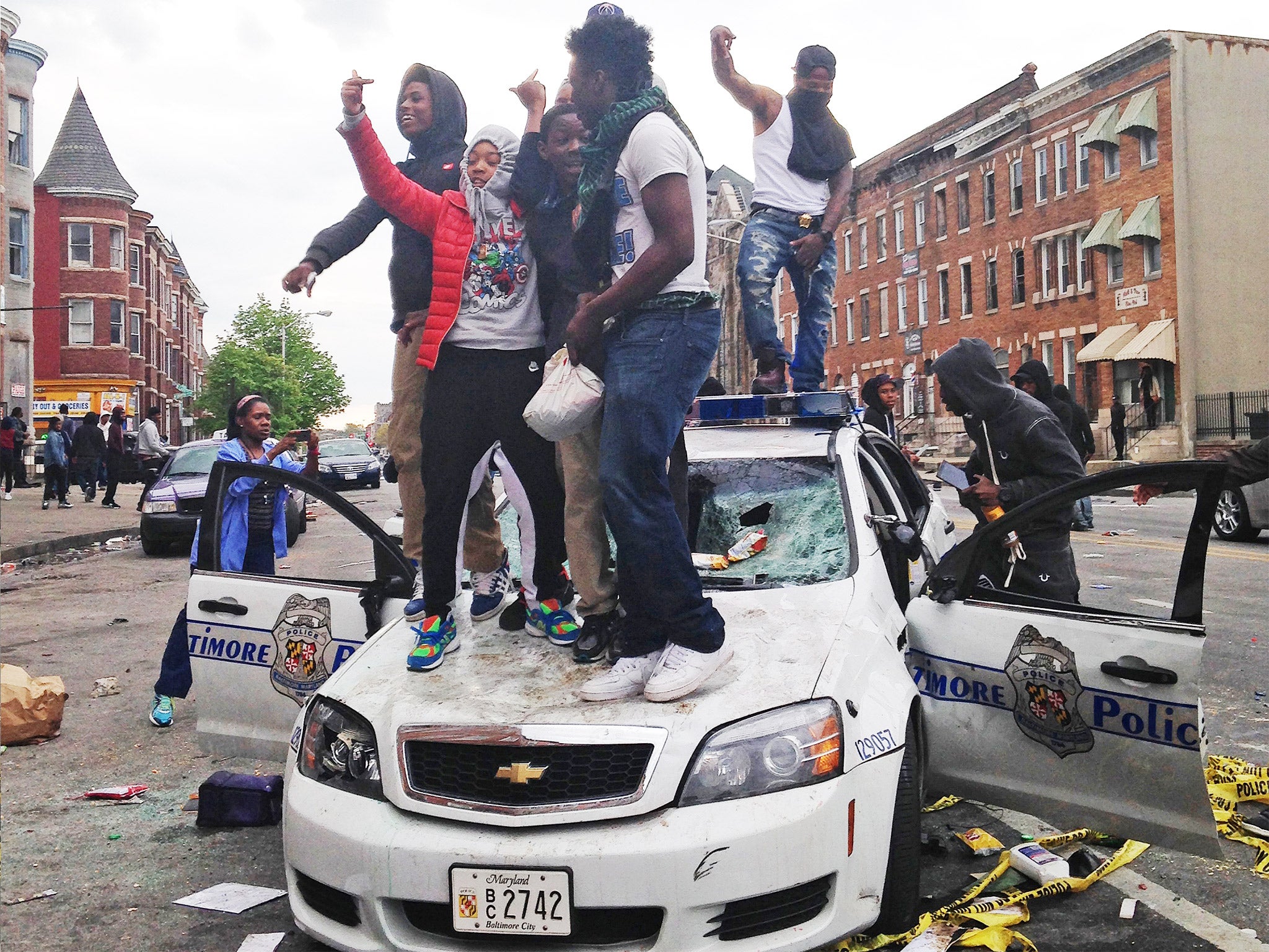 Protesters stand on top of a police car destroyed during Monday night's rioting