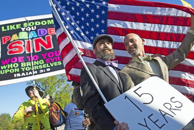 A gay couple hold an American flag in front of the Supreme Court in Washington, while a demonstrator holds a sign denouncing same-sex marriage