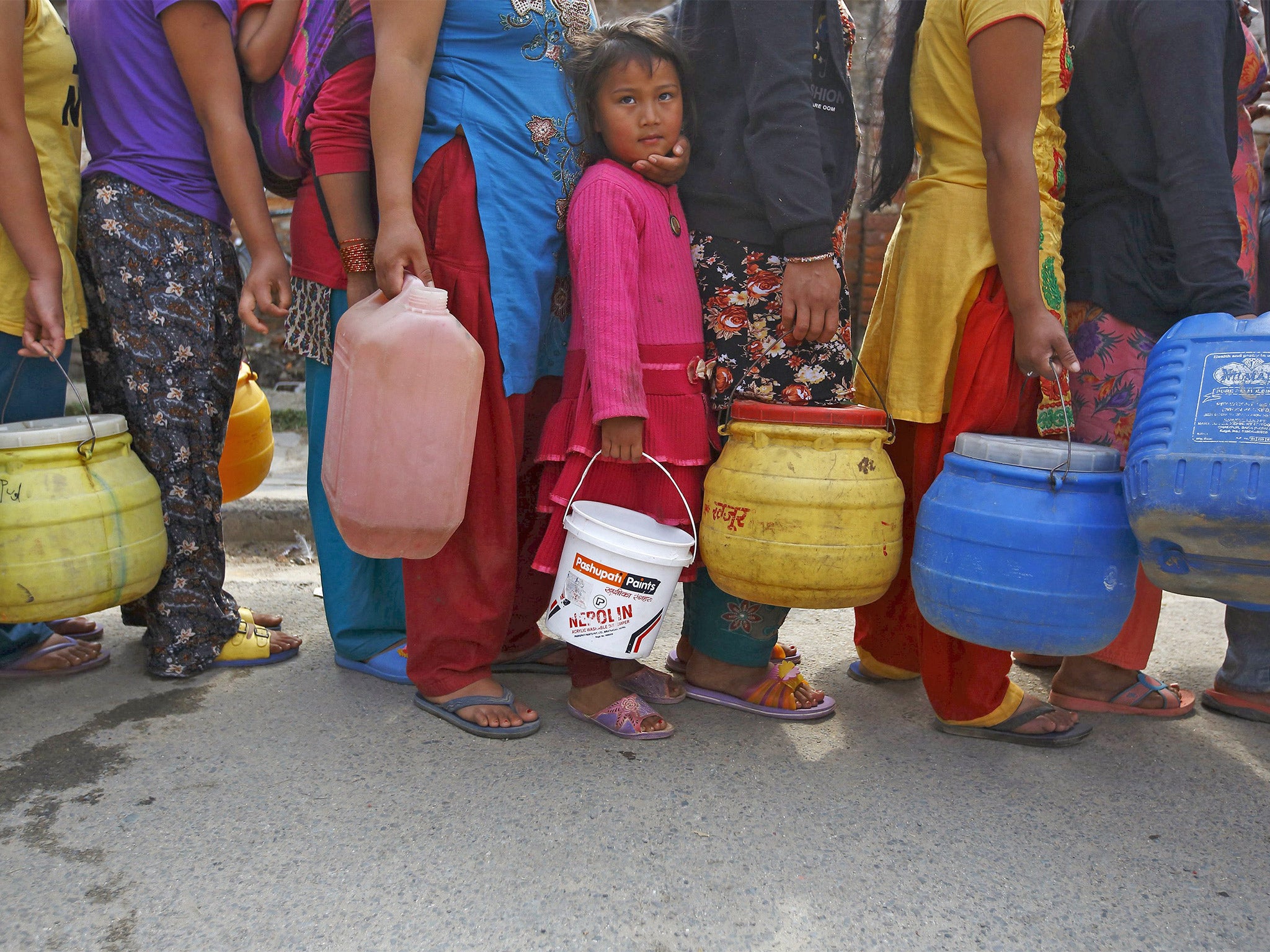 A girl stands in a queue to fill her container with water near the makeshift shelters in Kathmandu