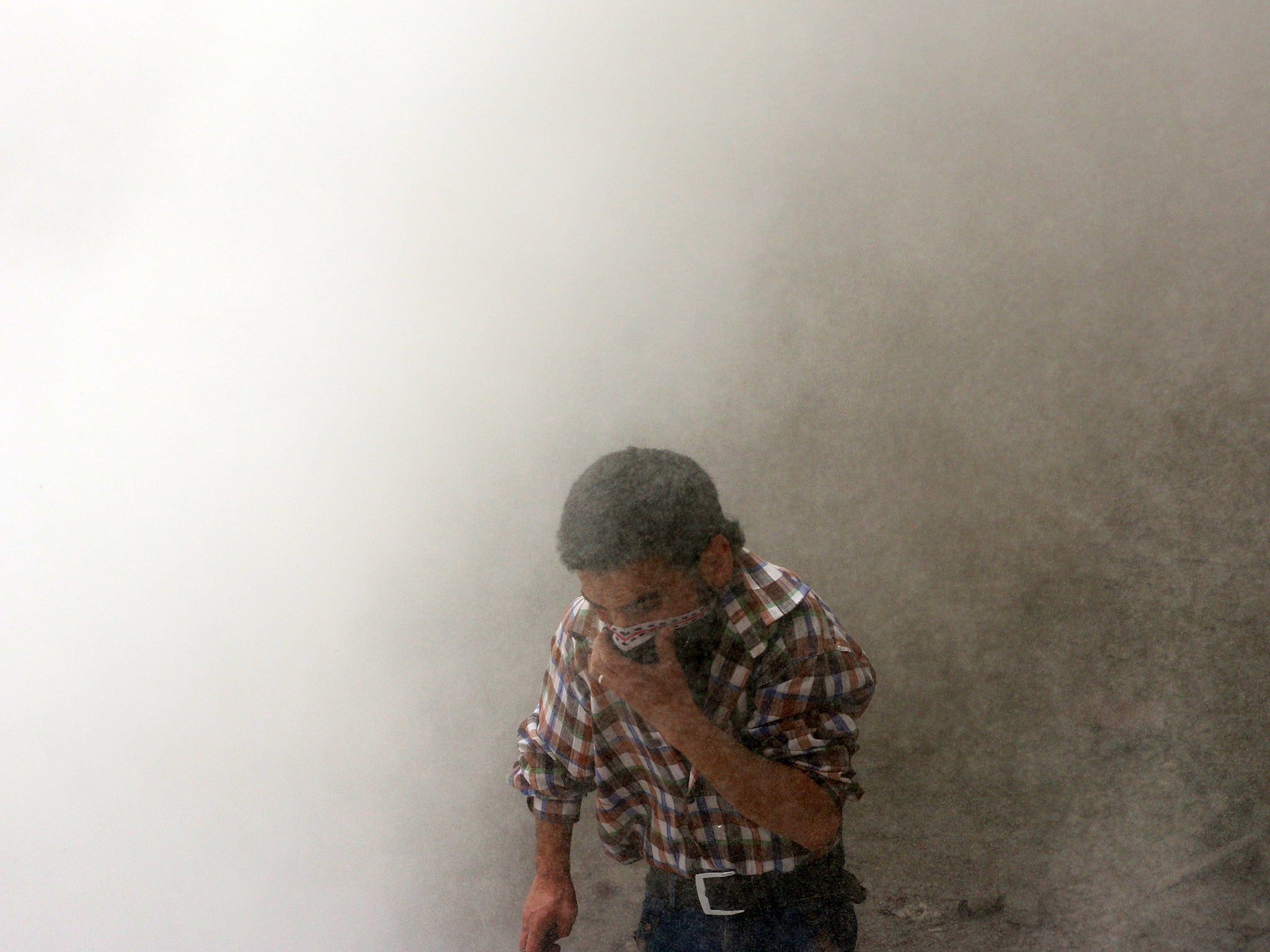 A man protects himself from dust following a reported barrel bomb attack by Syrian pro-government forces in Aleppo