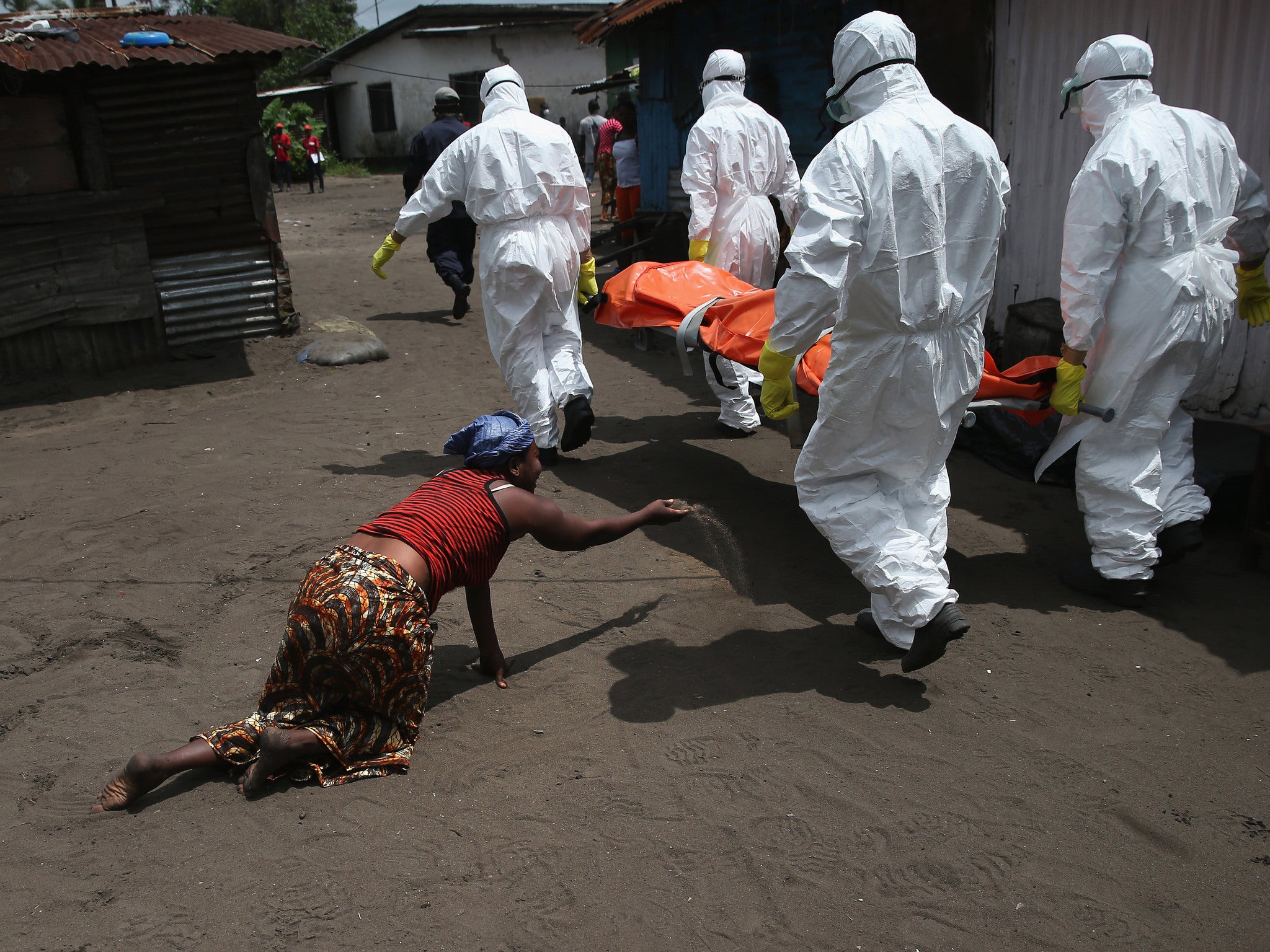 A woman throws a handful of soil towards the body of her sister as Ebola burial team members take her sister for cremation.