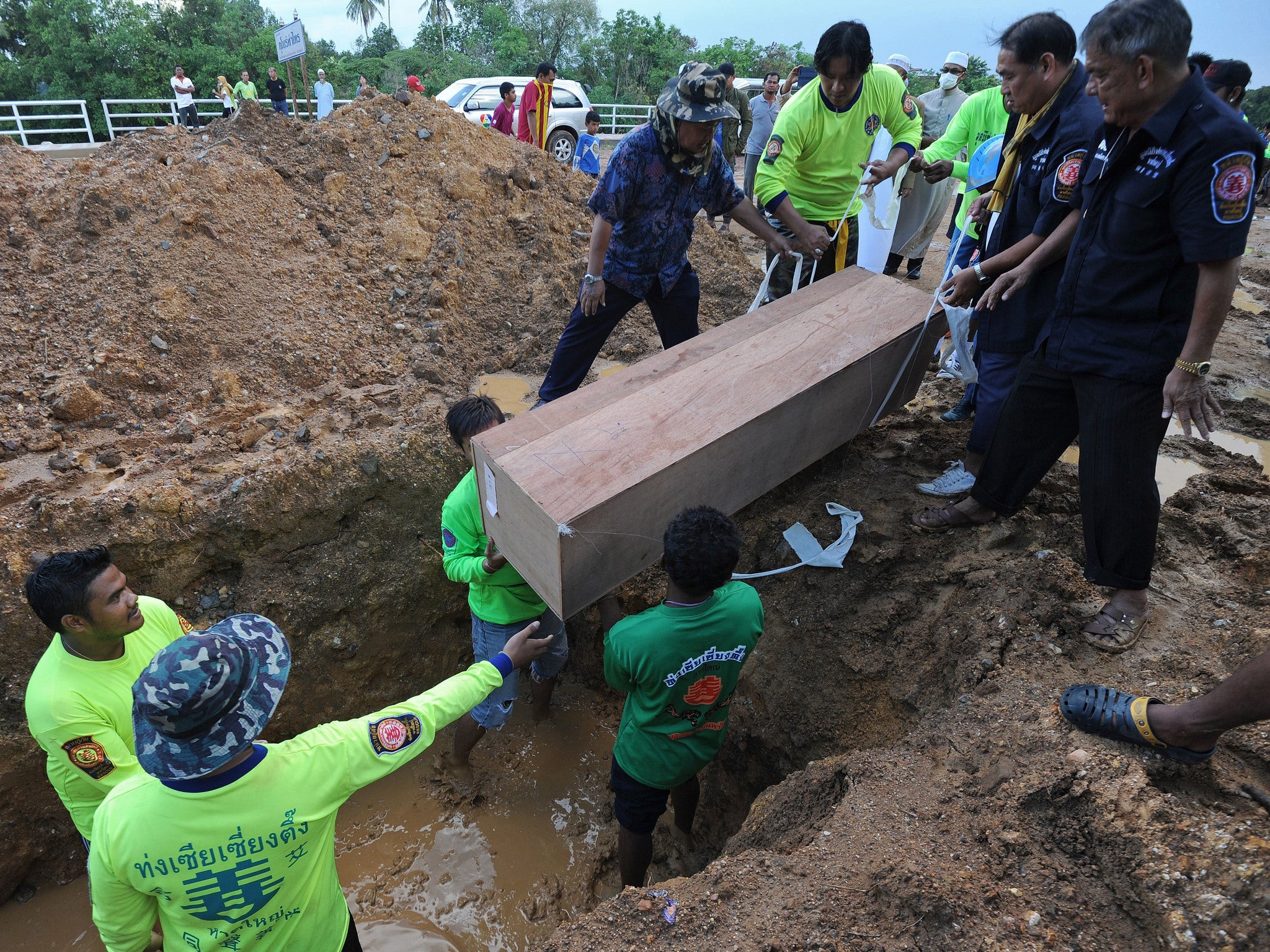 Rescue workers bury coffins containing the human remains of migrants exhumed the day before from a mass grave at an abandoned jungle camp in the Sadao district of Thailand's southern Songkhla province bordering Malaysia