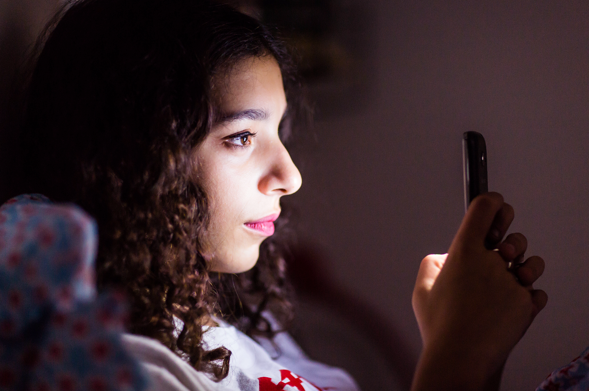 A teenage girl uses her smartphone in bed.