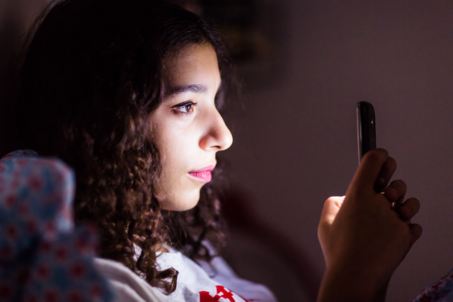 A teenage girl uses her smartphone in bed. 