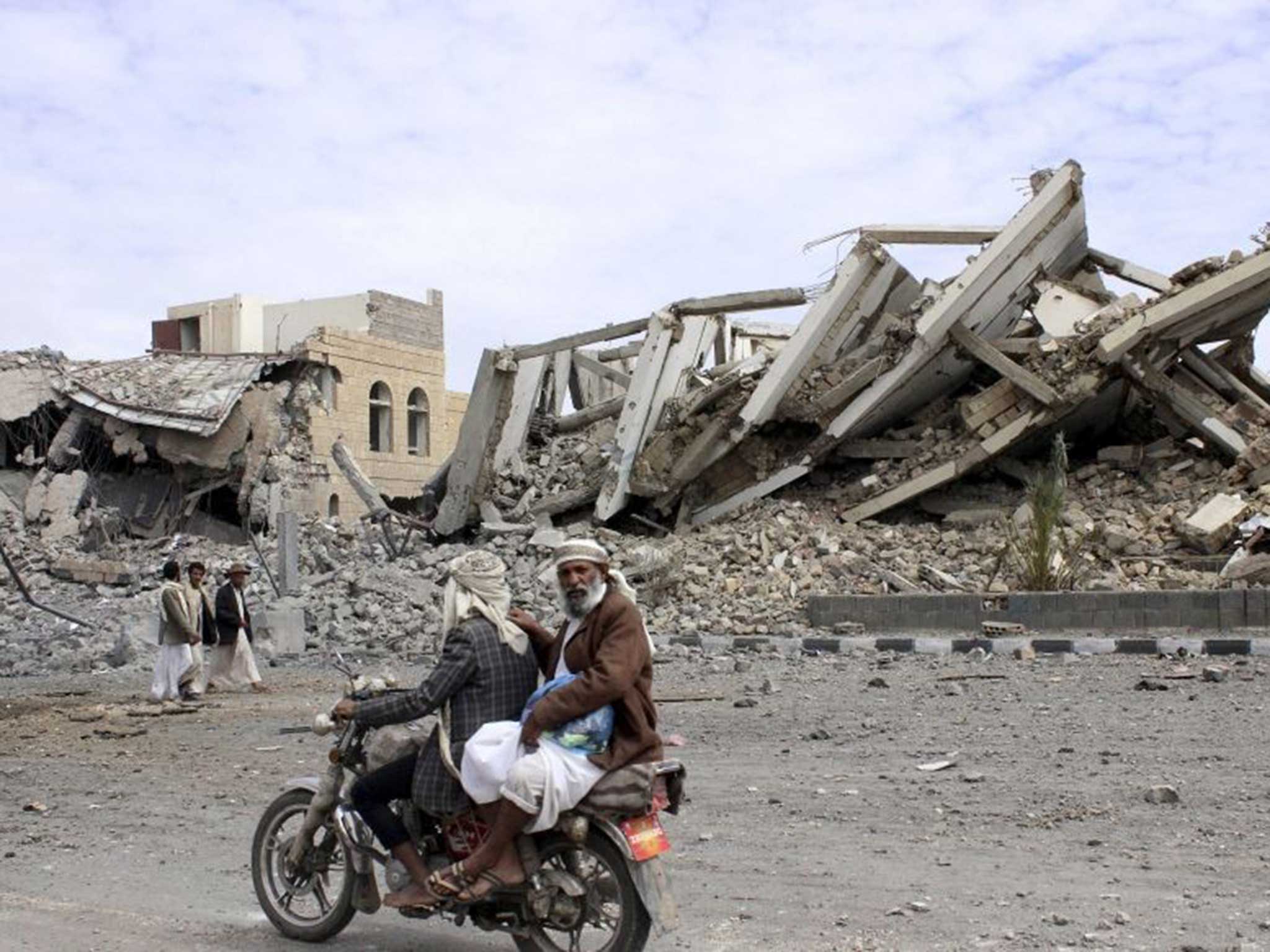 People ride on a motorcycle as they pass by a police headquarters destroyed by a Saudi-led air strike in Yemen's northwestern city of Saada