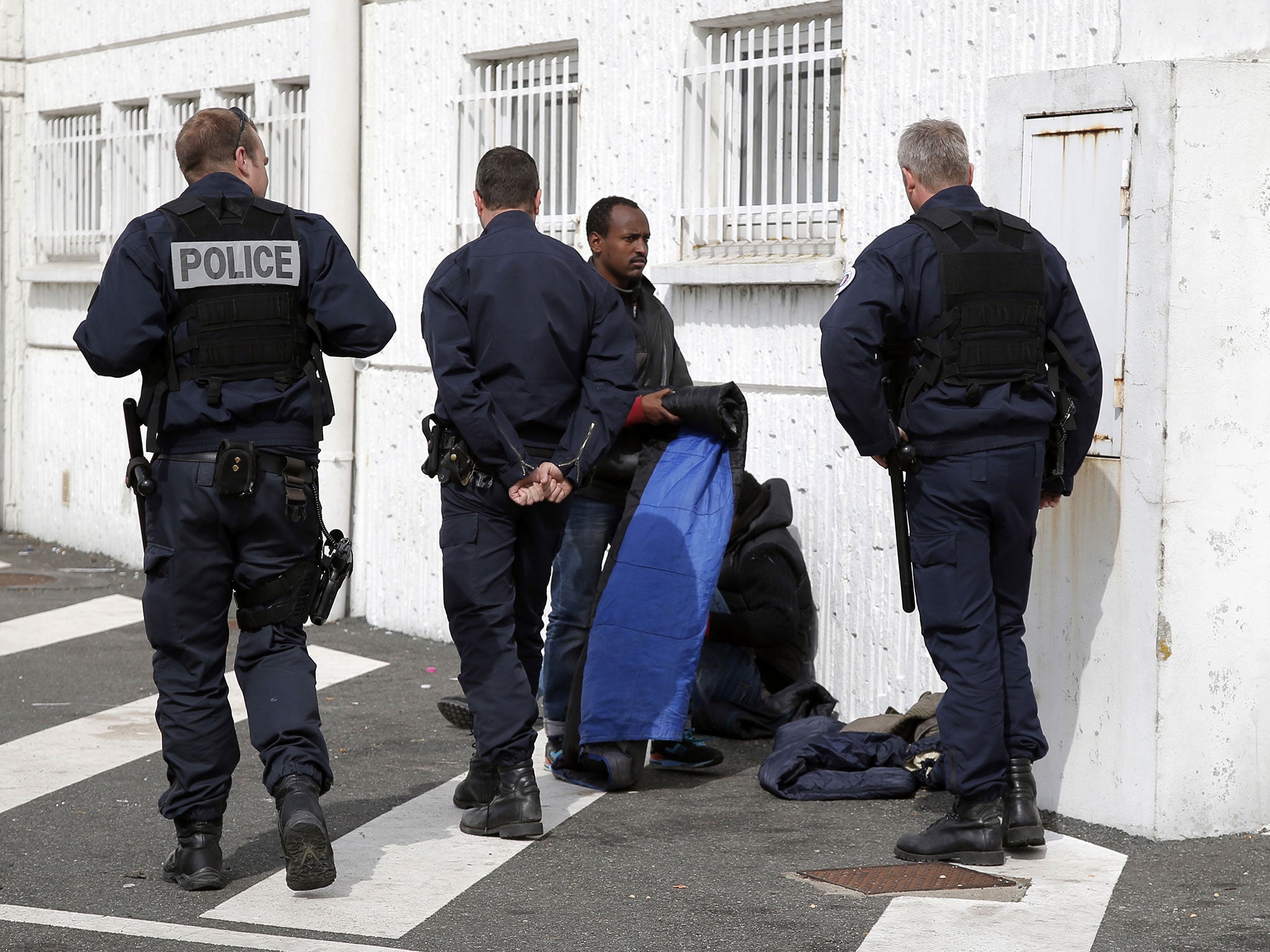French police officers ask migrants to move from the backyard of a supermarket