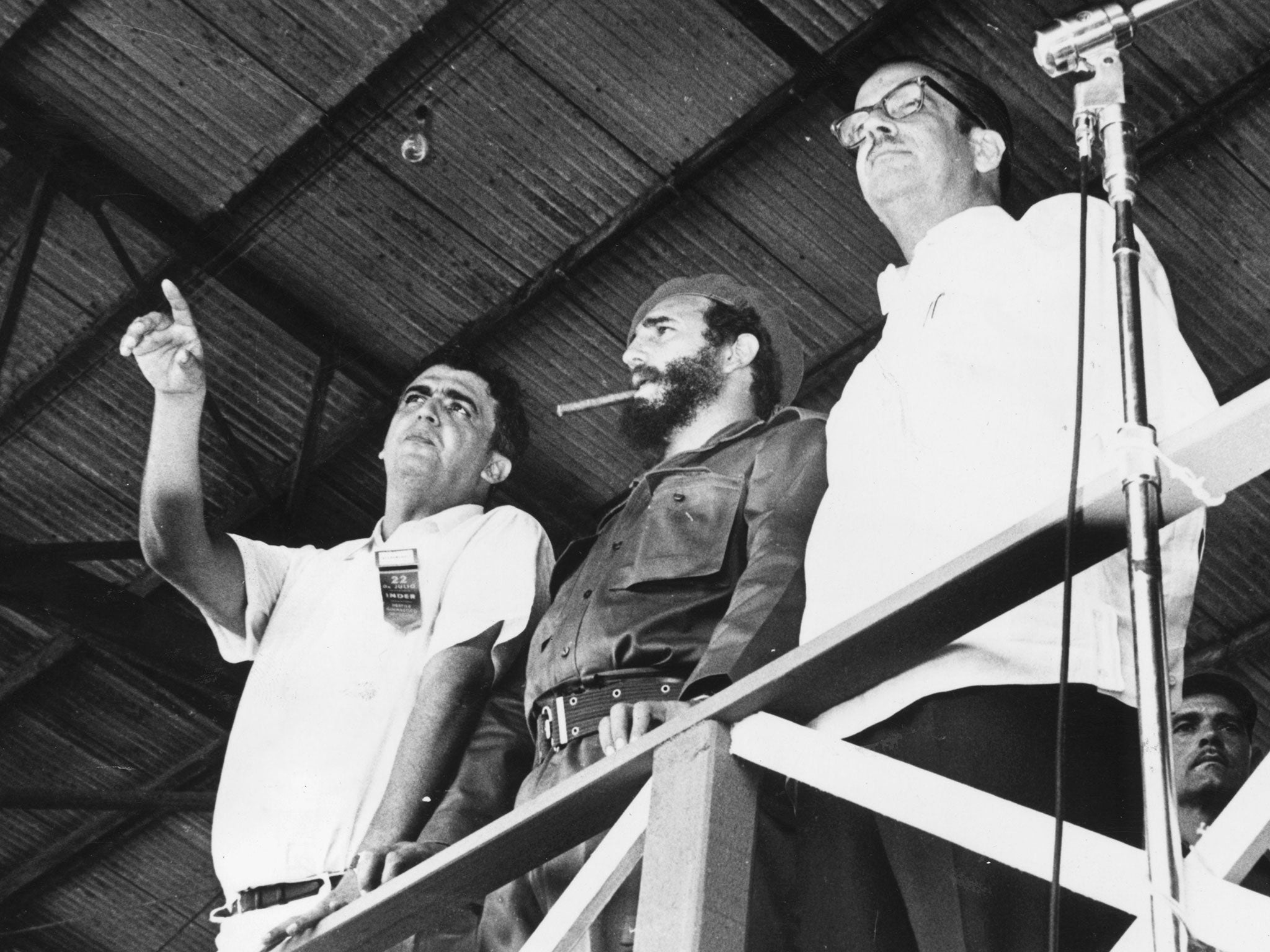 A young Fidel Castro, centre, smokes a cigar as he watches a Havana gymnastics festival in his then-role as Prime Minister in 1962