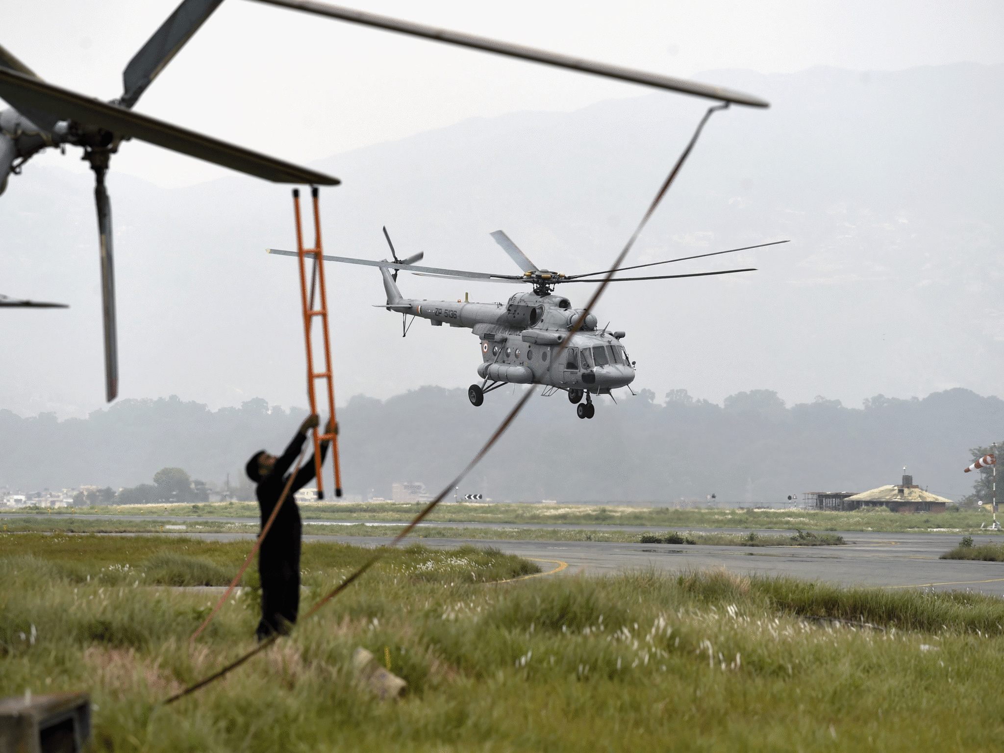 An Indian airforce crew member uses a ladder as he tries to tie down the rotor blade of a transport helicopter as another Indian aircraft lands at Kathmandu's International airport on May 7, 2015.