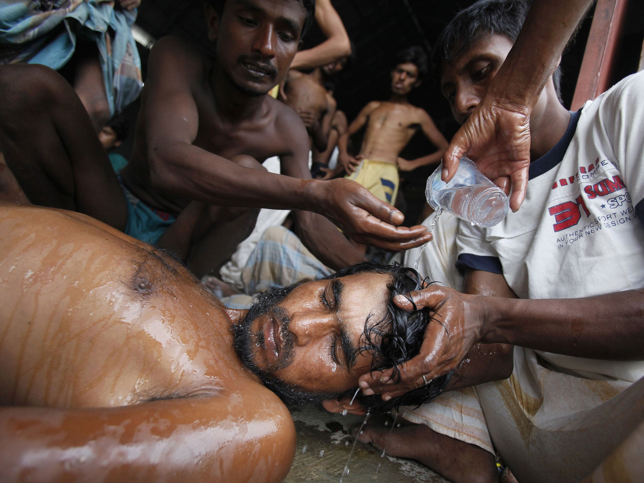 Newly arrived Bangladeshi migrants pour water on the head of a man who had fainted