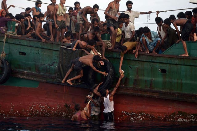 Rohingya migrants pass food supplies dropped by a Thai army helicopter to others aboard a boat drifting off the southern Thai island of Koh Lipe in the Andaman