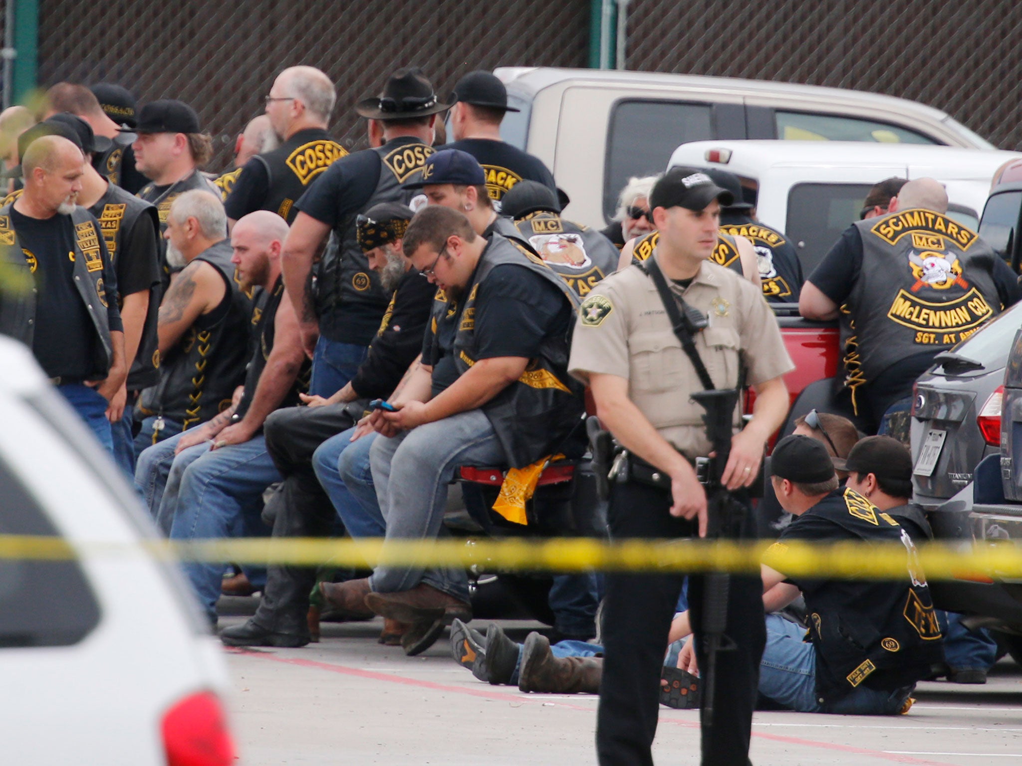 A McLennan County deputy stands guard near a group of bikers in the parking lot of a Twin Peaks restaurant in Waco, Texas. Police Sgt. W. Patrick Swanton told KWTX-TV there were 'multiple victims' after gunfire erupted between rival biker gangs at the restaurant
