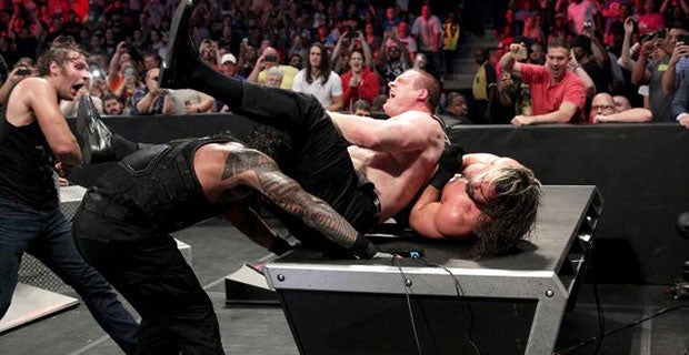 Reigns slams Kane down on top of Rollins