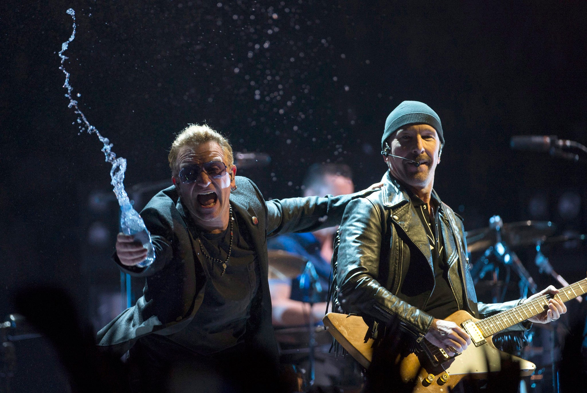 Bono throws water at the crowd while the Edge watches as they perform in the band's first concert of their new world tour in Vancouver