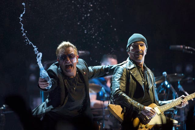 Bono throws water at the crowd while the Edge watches as they perform in the band's first concert of their new world tour in Vancouver
