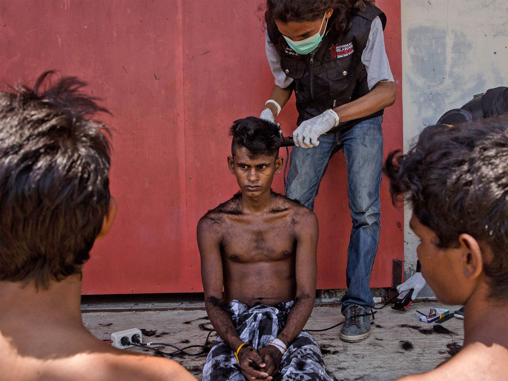 A volunteer cuts the hair of a Rohingya migrant at a temporary shelter in Kuala Langsa, Indonesia