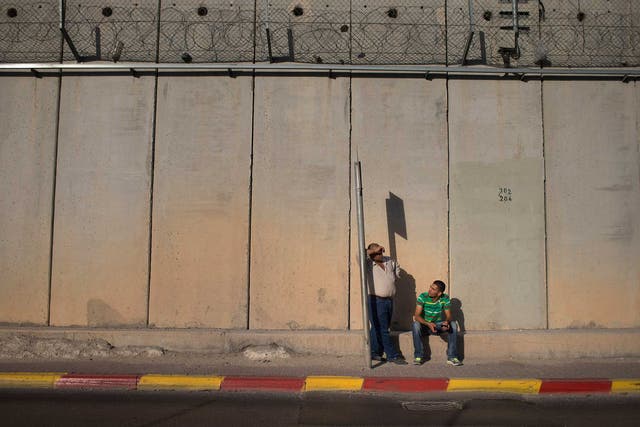 Two Palestinian men wait for a bus along the Isreali West Bank barrier in 2013
