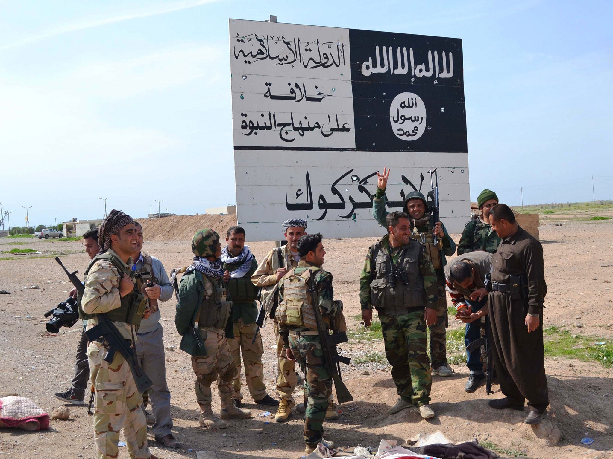 Kurdish Peshmerga fighters next to an Isis sign at the entrance to the northern Iraqi town of Hawija, south of Kirkuk, in March 2015. The battle for the town continues