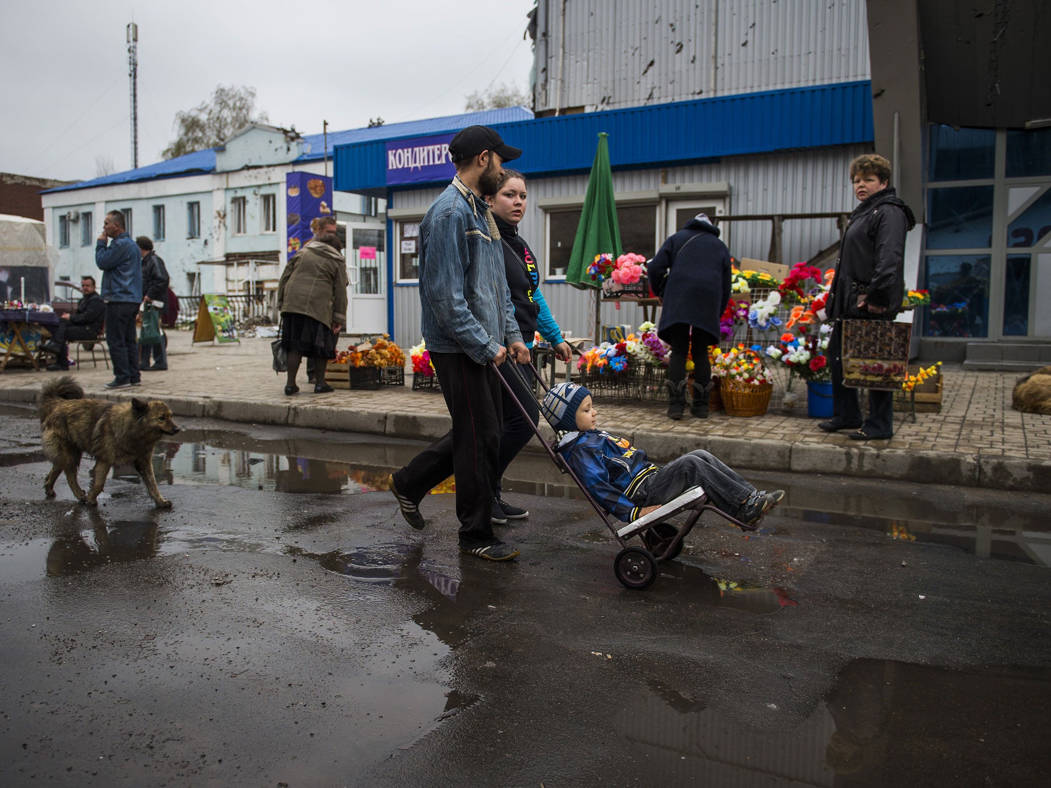 A family walks past a shrapnel damaged building and street vendors at a market by the railway station near the frontline in Donetsk