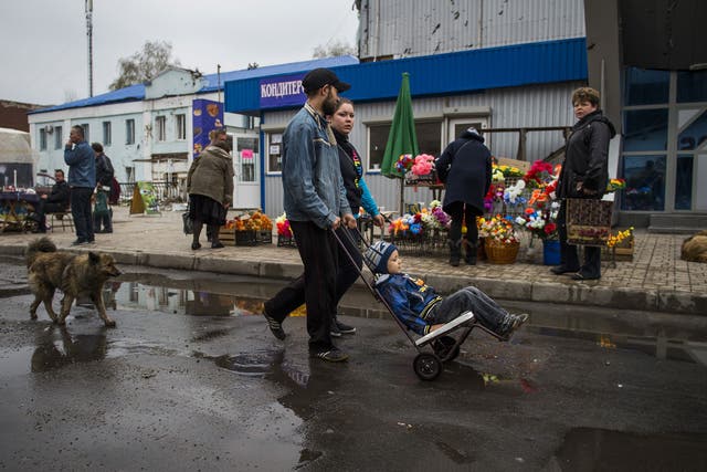 A family walks past a shrapnel damaged building and street vendors at a market by the railway station near the frontline in Donetsk 