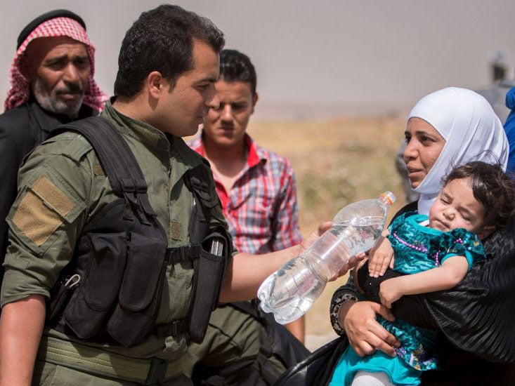 A Kurdish People's Protection Units (YPG) fighter offers water to a woman from Tel Tamr
