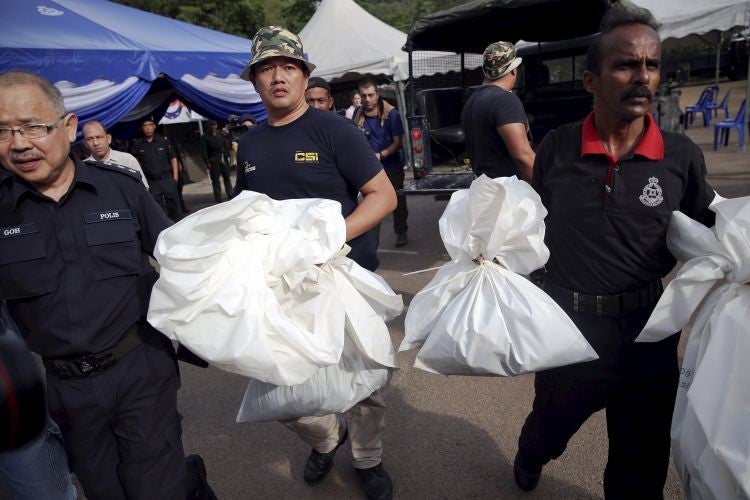 Forensic policemen carry body bags with human remains