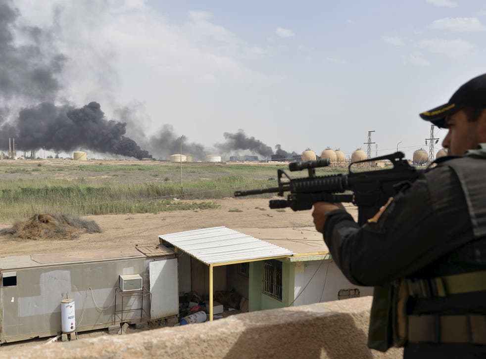 A member from the Iraqi security forces guards as smoke rises from Baiji oil refinery, north of Baghdad, Iraq May 26, 2015. Iraq's Shi'ite paramilitaries said on Tuesday they had taken charge of the campaign to drive Islamic State from the western provinc