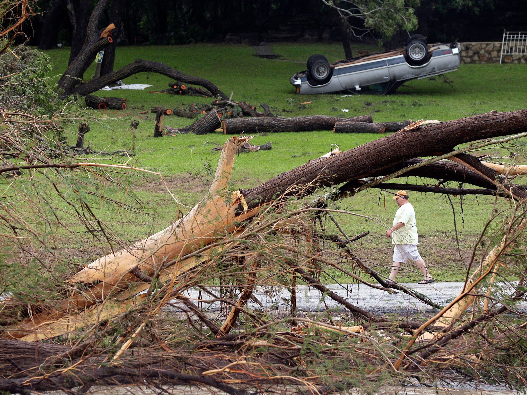 A man walks along the Blanco River where sweeping flood waters overturned vehicles and knocked down trees, in Wimberley