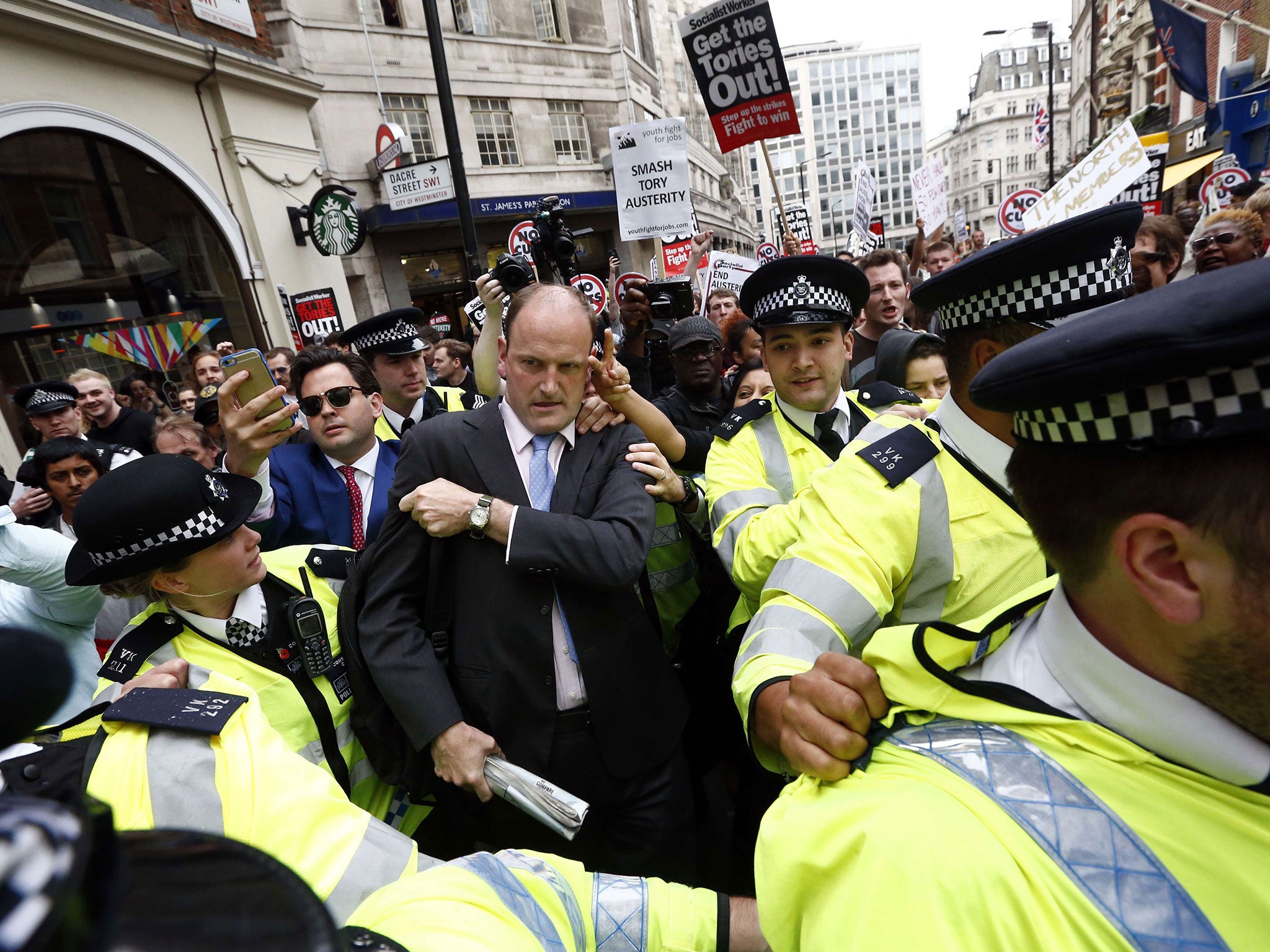 Police officers assist UKIP MP Douglas Carswell outside St James's Park underground station during an anti-austerity demonstration in London