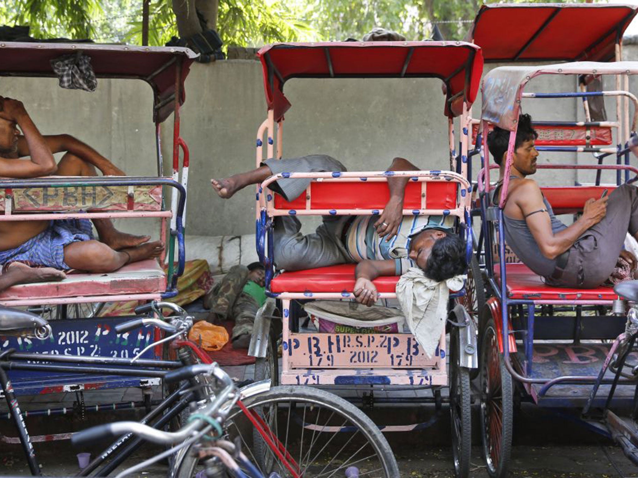 Rickshaw pullers sleep as they wait for the few customers venturing out in Delhi