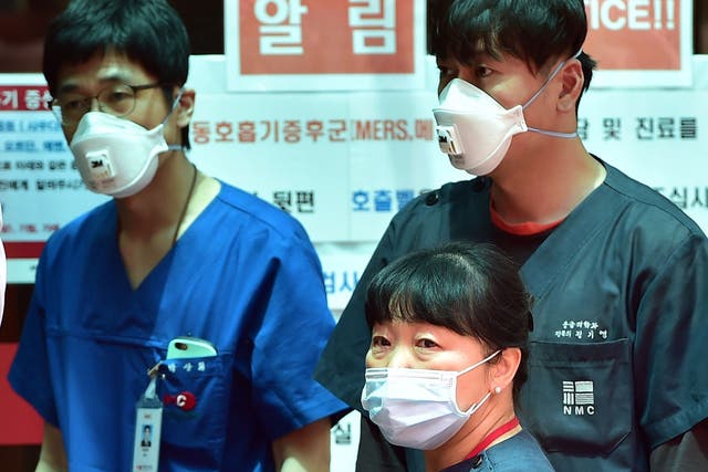 South Korean hospital workers wearing masks stand in front of a public notice on MERS while setting up a separated emergency center at the National Medical Center in Seoul